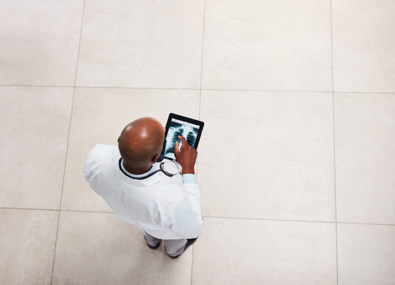 Buy stock photo High angle shot of a young doctor working on a digital tablet while standing inside of a hospital during the day