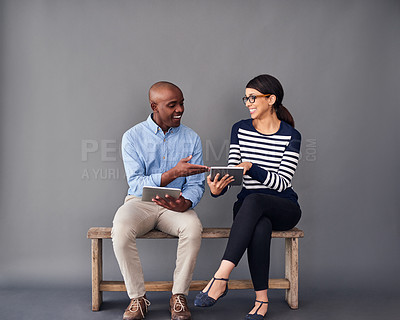 Buy stock photo Shot of two colleagues sitting next to each other while using digital tablets