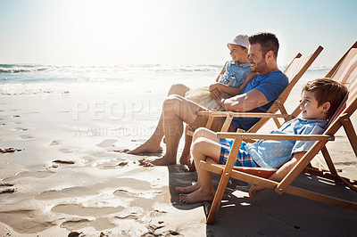 Buy stock photo Shot of a father and his two little children relaxing together on deck chairs at the beach