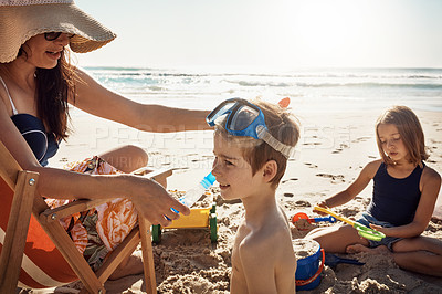 Buy stock photo Shot of a young woman putting snorkelling goggles on her son at the beach