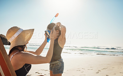 Buy stock photo Shot of a young woman putting snorkelling goggles on her daughter at the beach