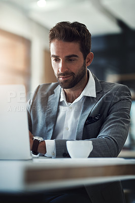 Buy stock photo Shot of a handsome young businessman using a laptop at his desk in a modern office