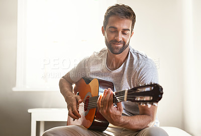 Buy stock photo Shot of a handsome young man playing a guitar at home