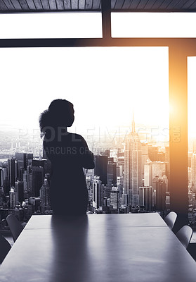 Buy stock photo Silhouetted shot of a young businesswoman looking at a cityscape from an office window