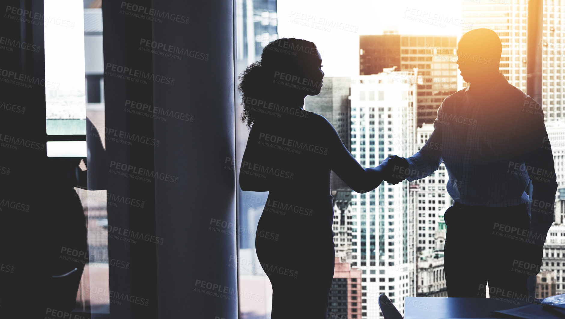 Buy stock photo Silhouetted shot of two businesspeople shaking hands in an office