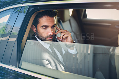 Buy stock photo Shot of a confident young businessman texting on his phone while being seated in the backseat of a car