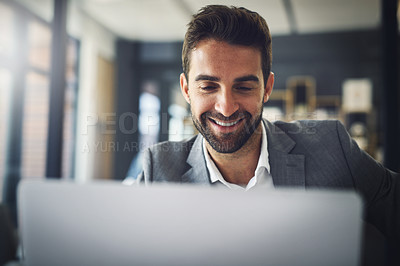 Buy stock photo Shot of a cheerful young businessman working on his laptop while being seated in the office during the day
