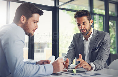 Buy stock photo Shot of two young businessmen working through business plans together inside of the office