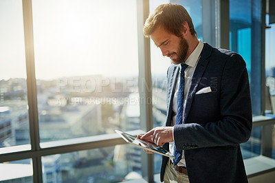 Buy stock photo Cropped shot of a handsome young businessman using a tablet in his office