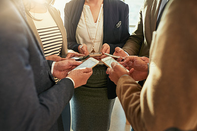 Buy stock photo Cropped shot of a group of businesspeople using their cellphones while standing in a huddle