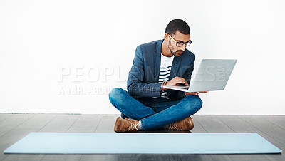 Buy stock photo Studio shot of a young man sitting on the floor and using a laptop while working on blank paper