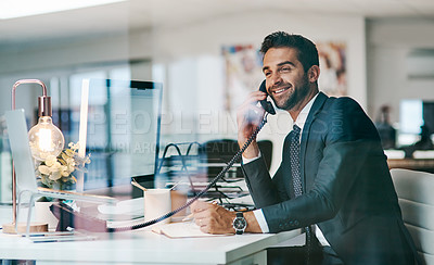 Buy stock photo Shot of a cheerful young businessman making a call while being seated inside of the office
