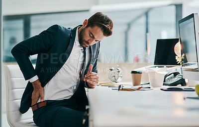Buy stock photo Shot of a uncomfortable young businessman holding his back in discomfort due to pain while being sated in the office