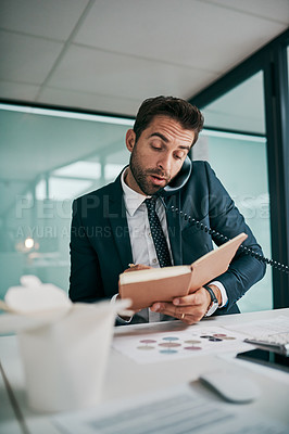 Buy stock photo Shot of a focused young businessman talking on the phone while writing in a notebook at the office