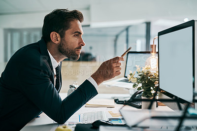 Buy stock photo Shot of a focused young businessman pointing at a computer screen with a pen while being seated in the office during the day