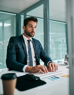Buy stock photo Shot of a focused young businessman working on his computer and typing while being seated in the office