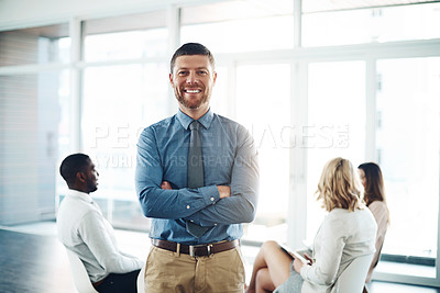 Buy stock photo Cropped portrait of a handsome young businessman standing with his arms folded during a meeting in the office