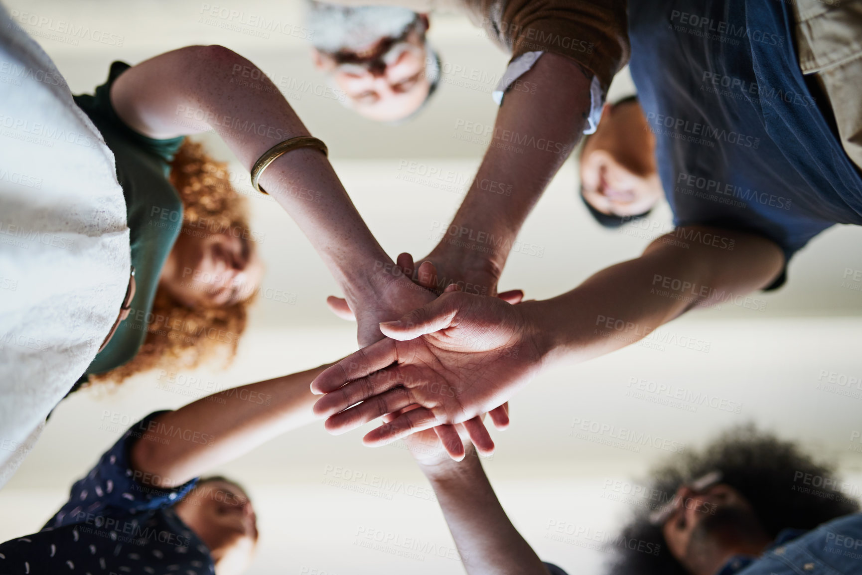 Buy stock photo Low angle shot of a group of cheerful creative businesspeople forming a huddle with their hands inside of the office