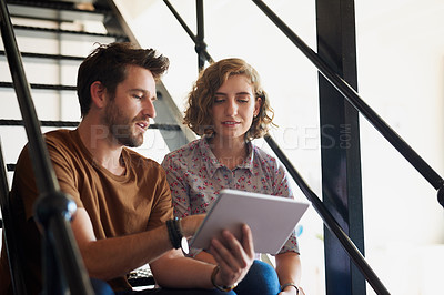Buy stock photo Shot of two designers discussing something on a tablet while sitting on a staircase