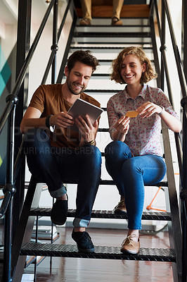 Buy stock photo Shot of two designers discussing something on a tablet while sitting on a staircase