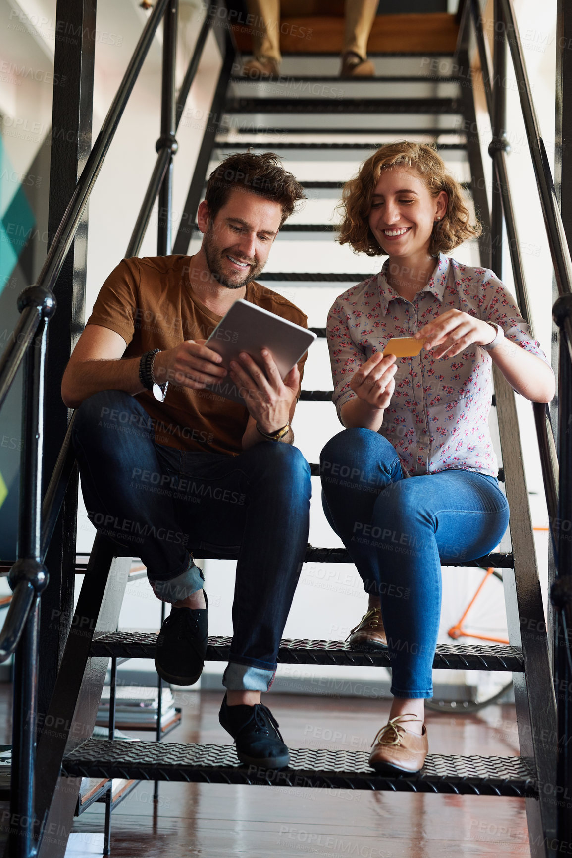 Buy stock photo Shot of two designers discussing something on a tablet while sitting on a staircase
