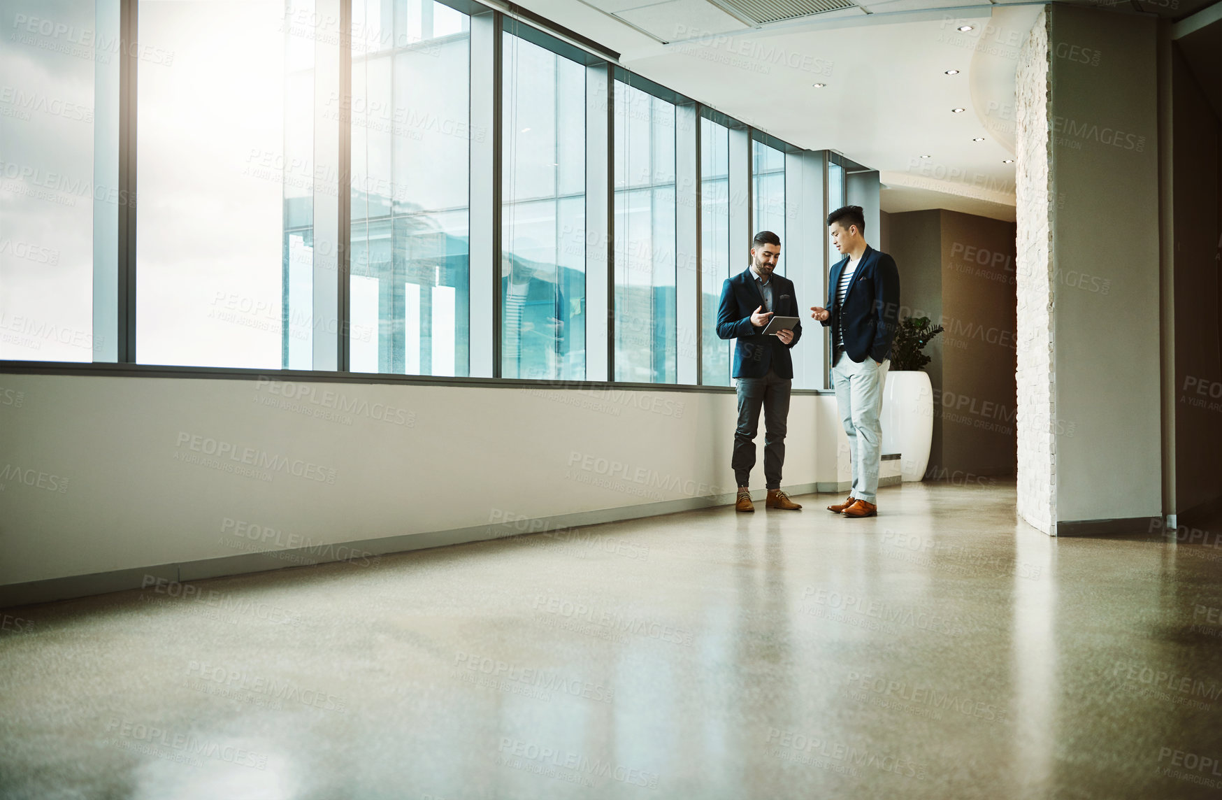 Buy stock photo Shot of two young businessmen using a digital tablet together in a modern office