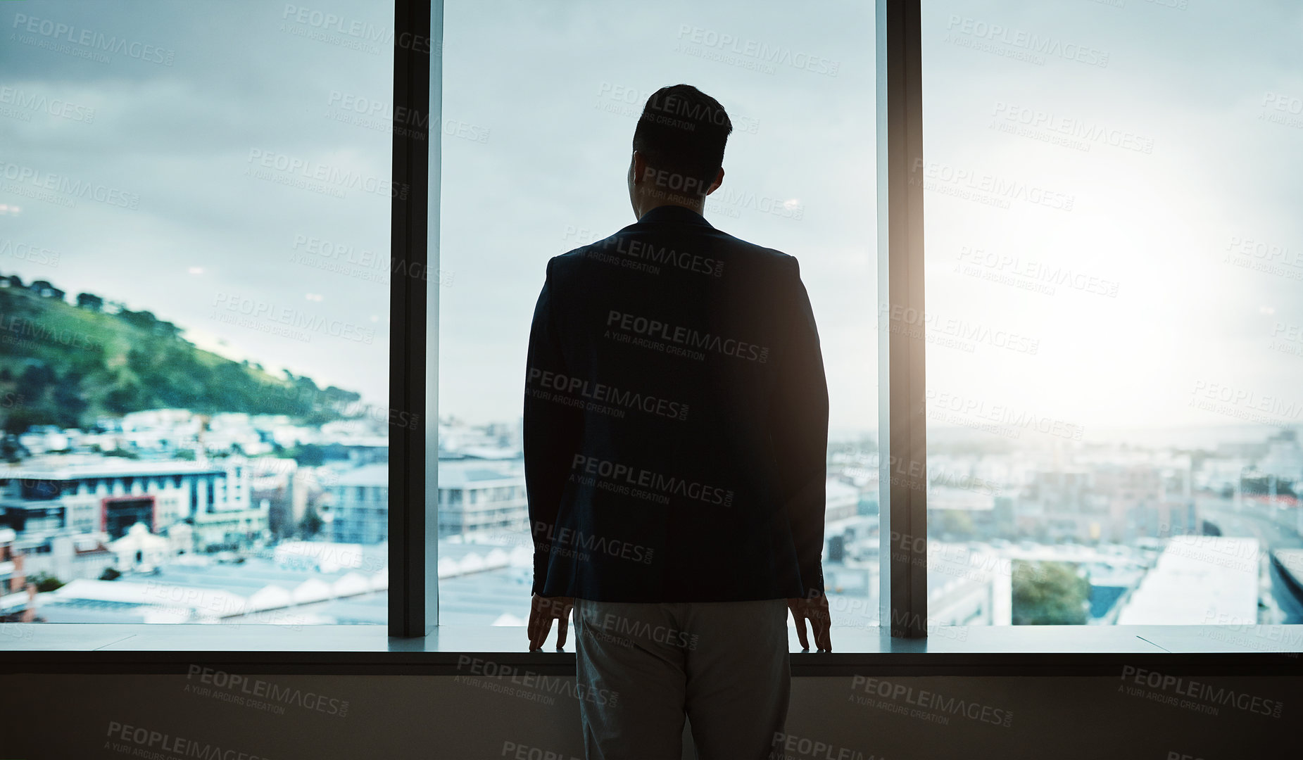 Buy stock photo Rearview shot of a young businessman looking thoughtfully out of an office window