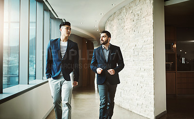 Buy stock photo Shot of two young businessmen walking and talking in a modern office
