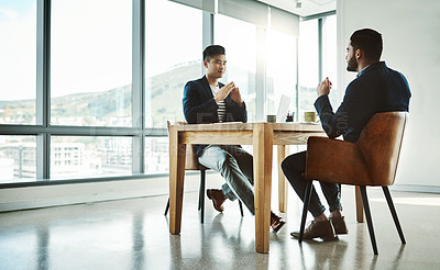 Buy stock photo Shot of two young businessmen having a discussion at a desk in a modern office