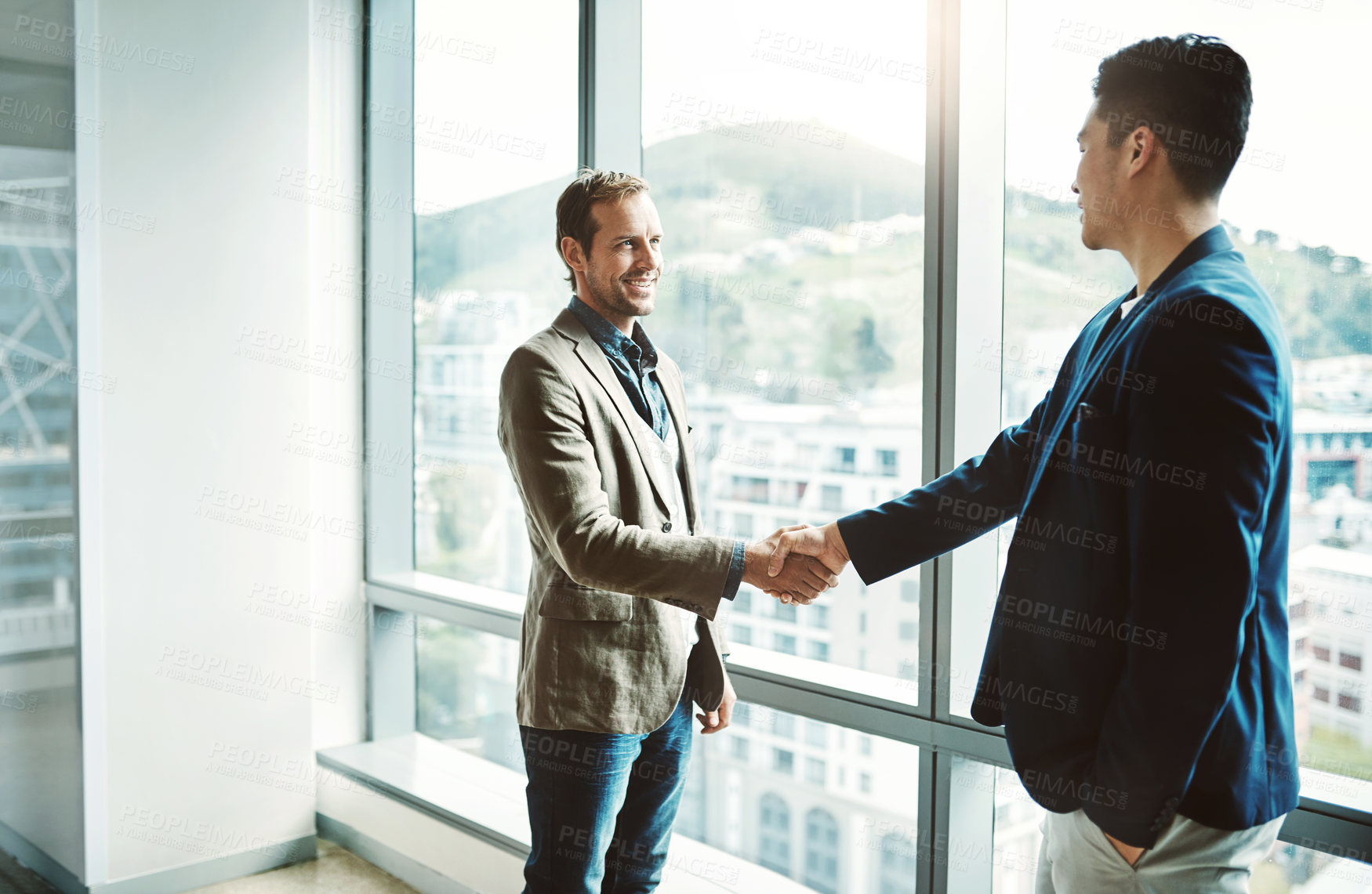 Buy stock photo Shot of two confident businessmen shaking hands in agreement while standing inside the office during the day