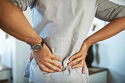Buy stock photo Rearview shot of an unrecognizable man holding his back in discomfort due to pain inside at home