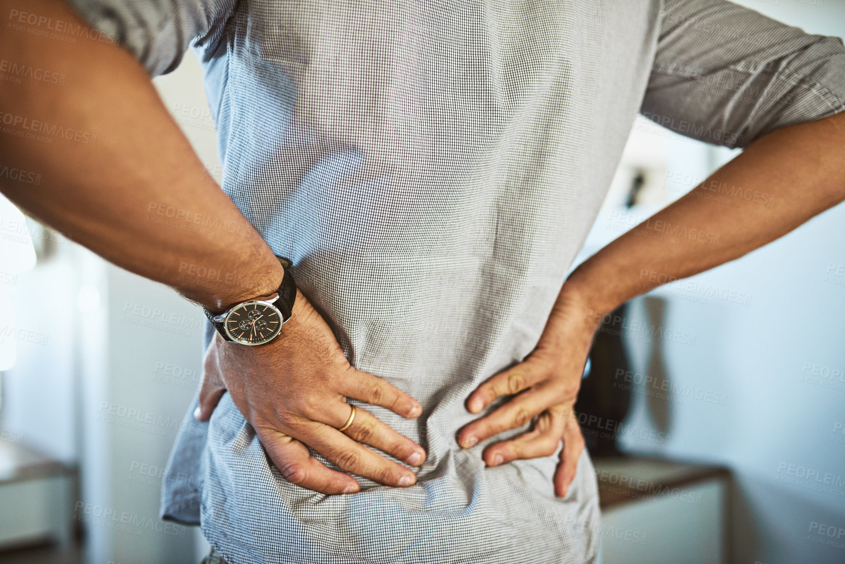 Buy stock photo Rearview shot of an unrecognizable man holding his back in discomfort due to pain inside at home