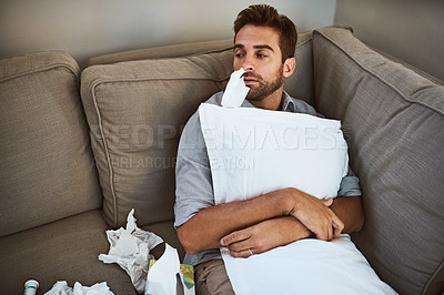 Buy stock photo Shot of a tired young man lying on a couch with a tissue in his nose and holding a pillow at home during the day