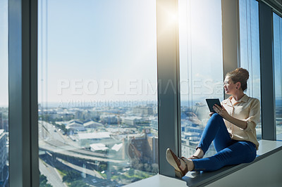 Buy stock photo Shot of cheerful young businesswoman browsing on a digital tablet while being seated next to a window and looking through it