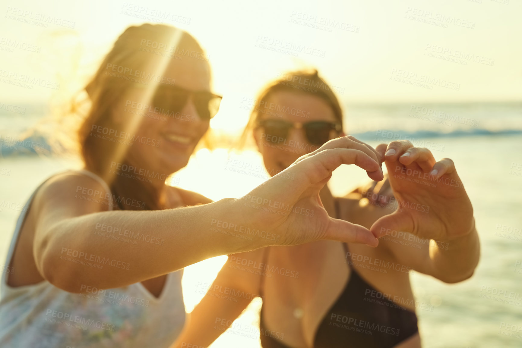 Buy stock photo Hand heart, lgbtq and couple at beach for summer vacation, bonding and travel together in Miami. Smile, women and love sign with embrace in sunshine for sunglasses, date support and relationship care