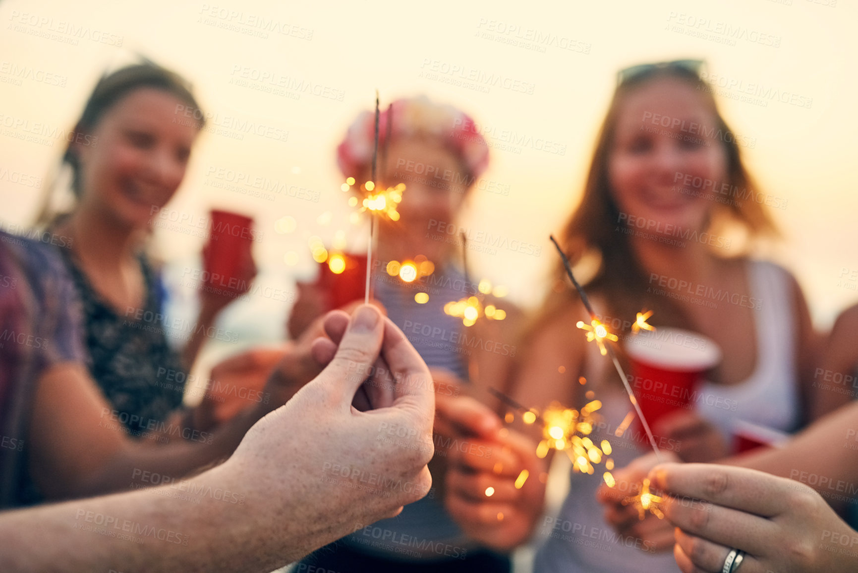 Buy stock photo Hand, sparklers and beach with happy friends at sunset party for summer, vacation or holiday in nature together. New years, drinks and celebration with people, bonding and drinking by Miami sea