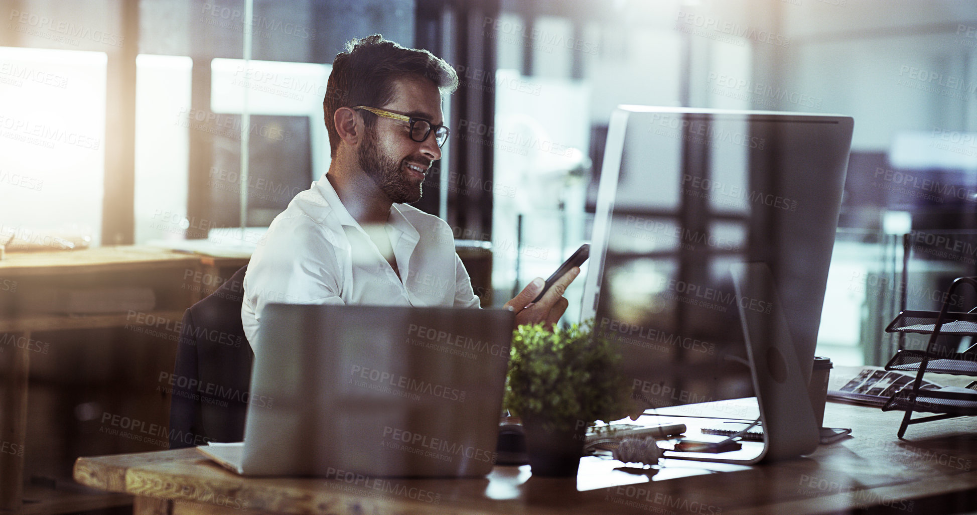 Buy stock photo Cropped shot of a handsome young businessman using his cellphone while working late in the office