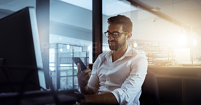 Buy stock photo Cropped shot of a handsome young businessman using his cellphone while working late in the office