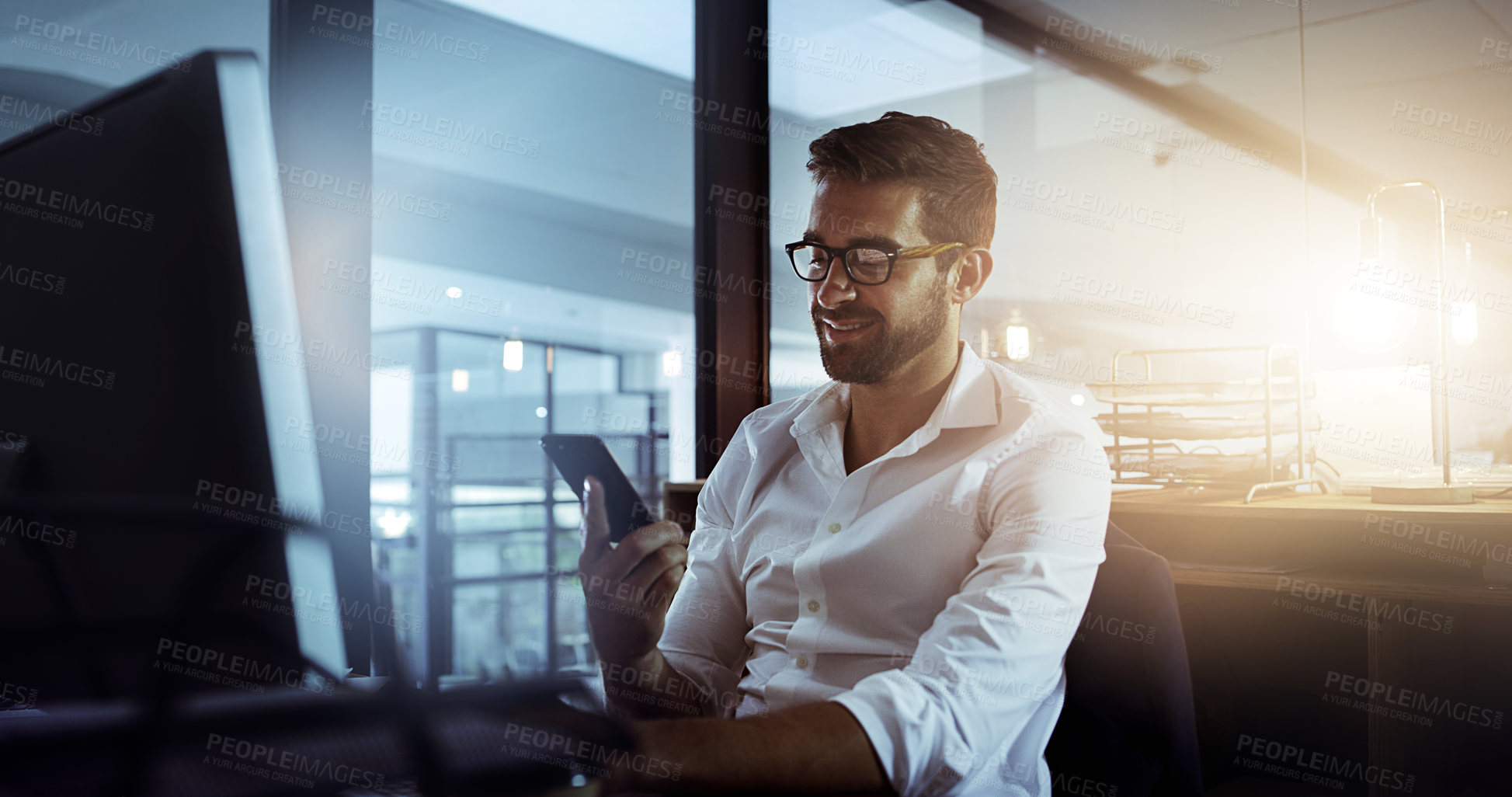 Buy stock photo Cropped shot of a handsome young businessman using his cellphone while working late in the office