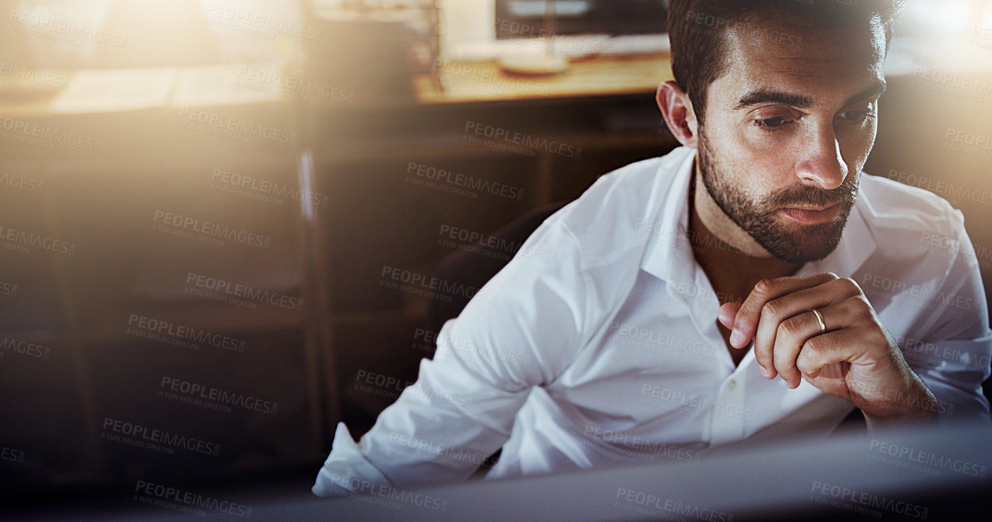 Buy stock photo High angle shot of a handsome young businessman looking thoughtful while working late in the office