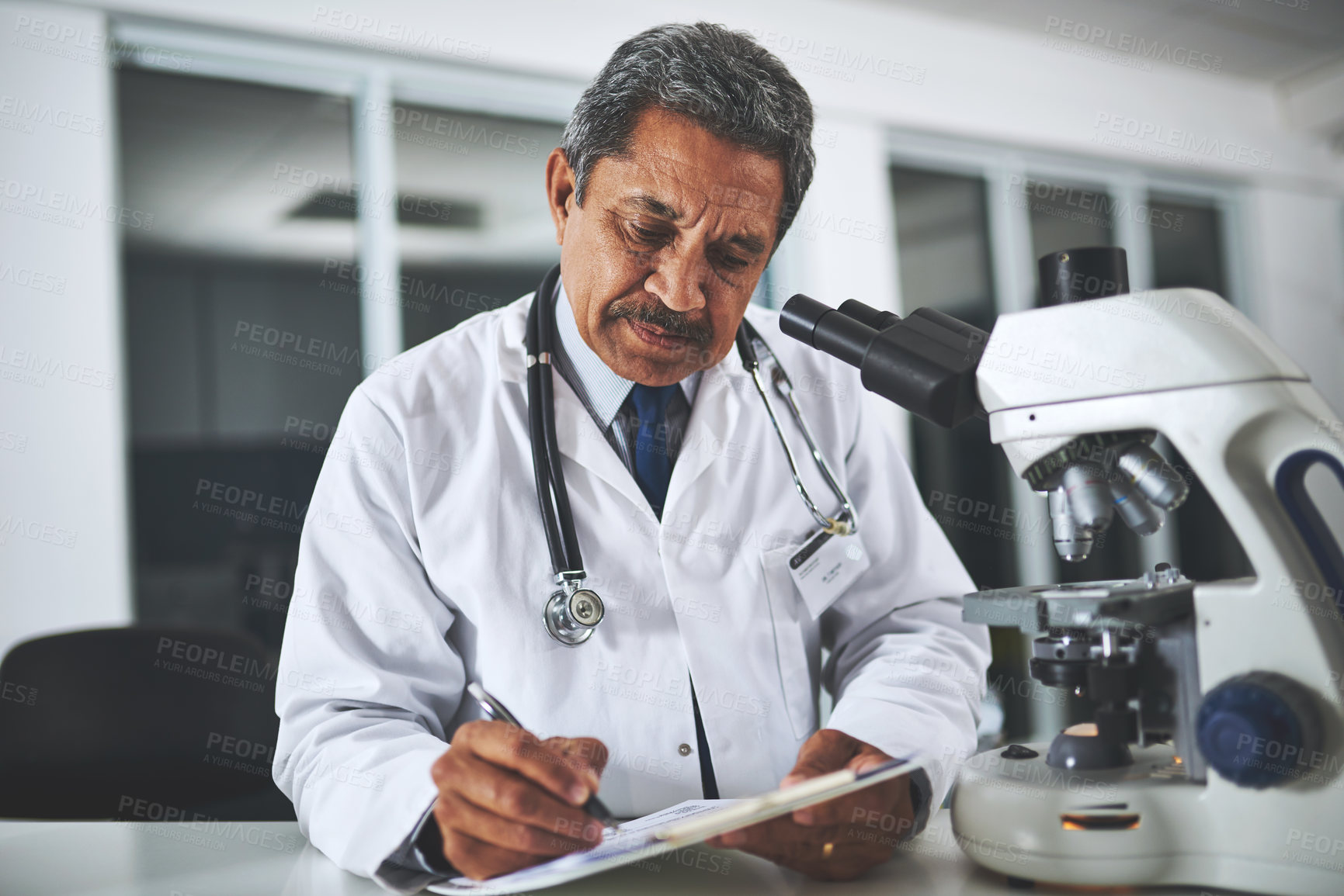 Buy stock photo Shot of a mature scientist using a microscope and recording his findings in a laboratory