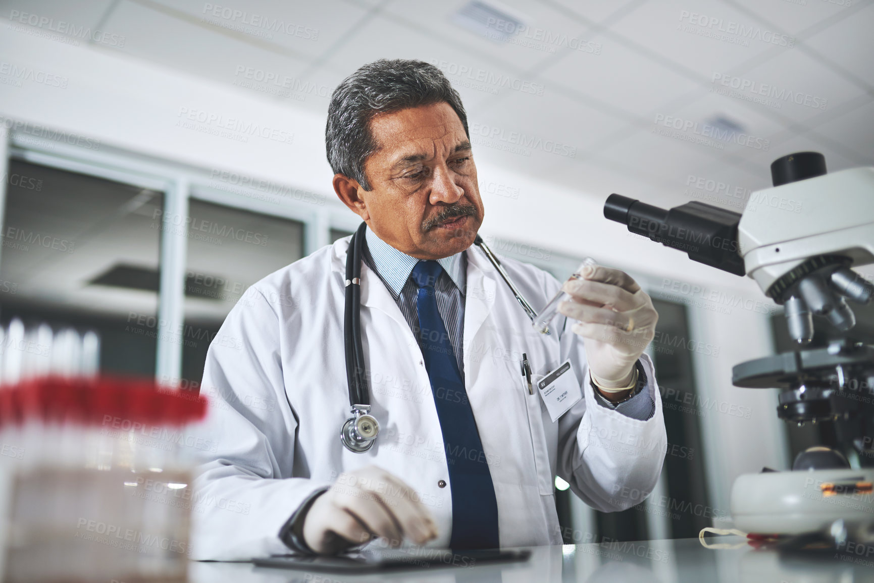 Buy stock photo Shot of a mature scientist examining liquid in a test tube in a laboratory