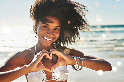 Buy stock photo Portrait of a beautiful young woman making a heart shaped gesture with her hands at the beach