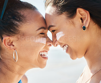 Buy stock photo Shot of two beautiful young women at the beach with sunscreen on their faces smiling at each other