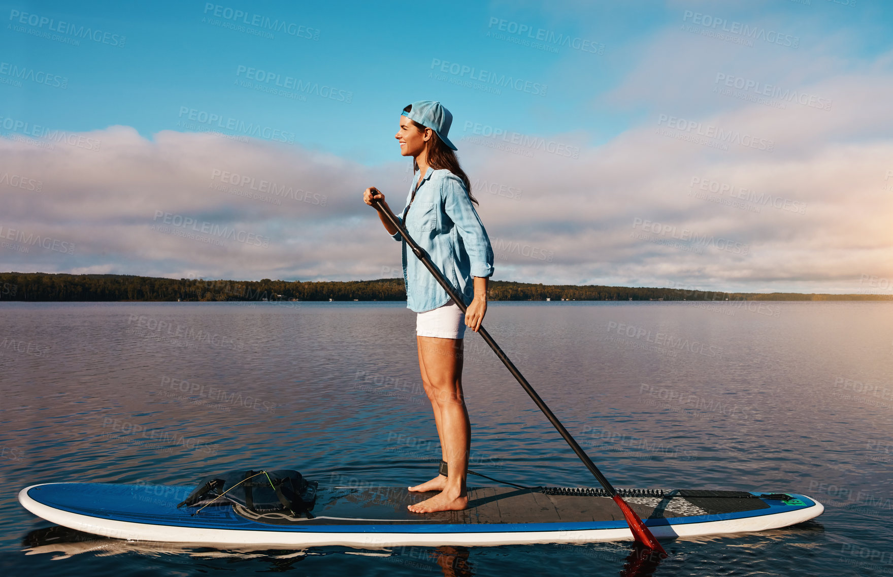 Buy stock photo Shot of a young woman paddle boarding on a lake