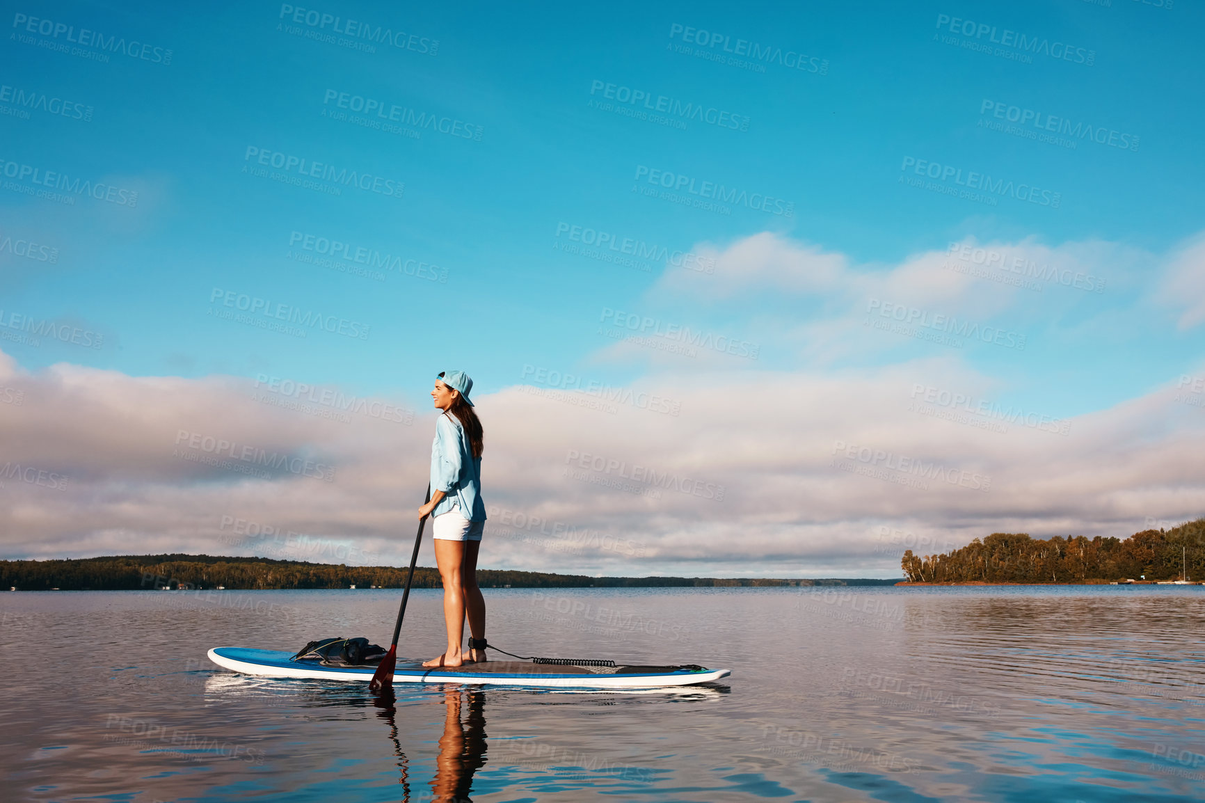 Buy stock photo Shot of a young woman paddle boarding on a lake