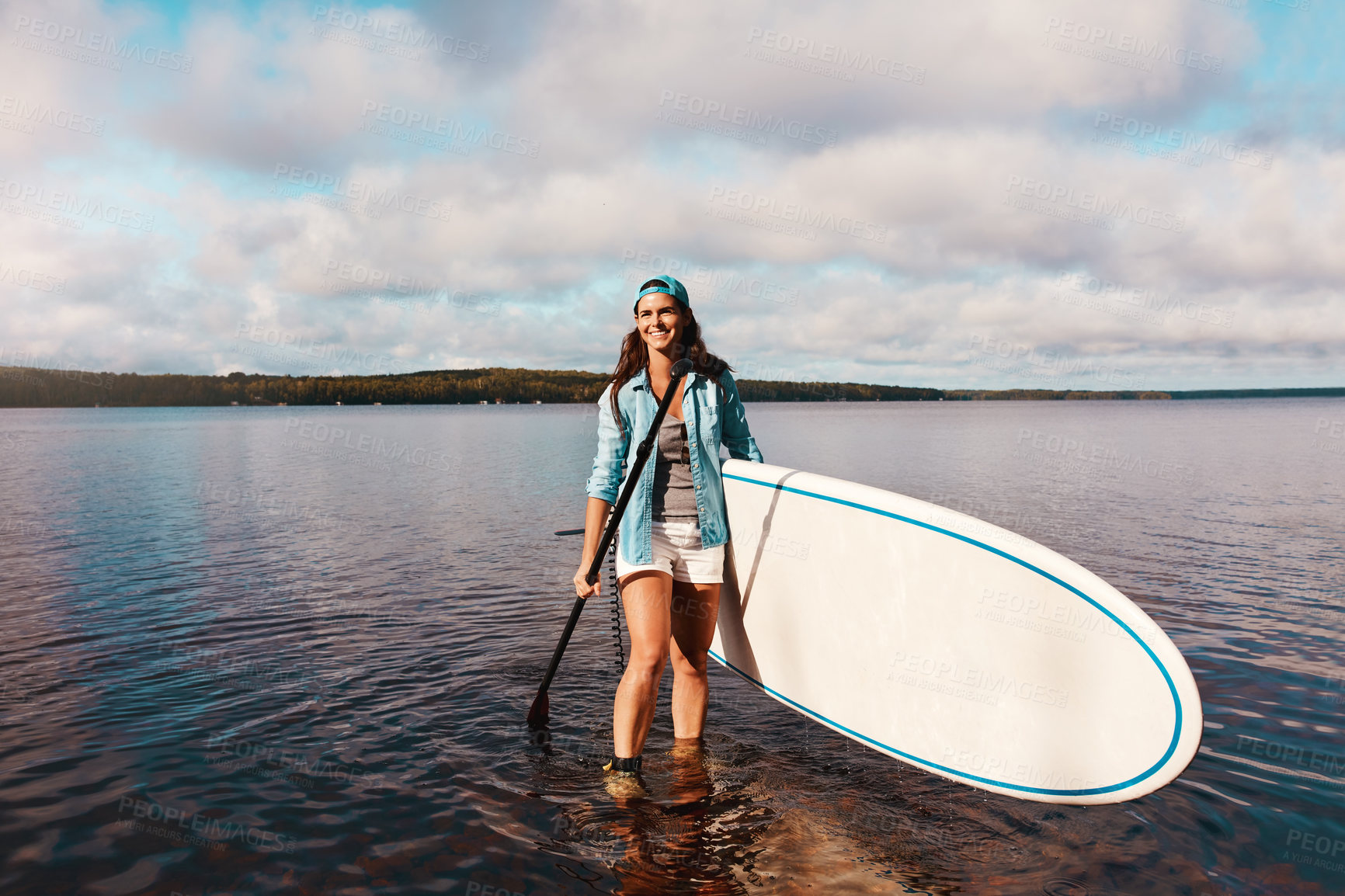 Buy stock photo Shot of a young woman paddle boarding on a lake