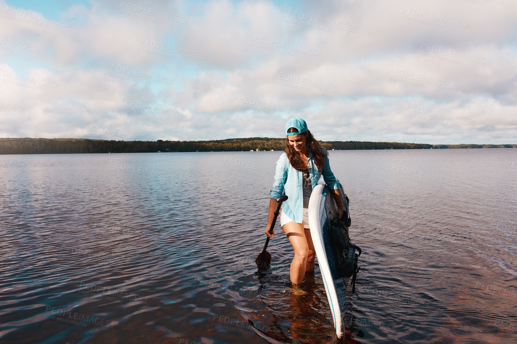 Buy stock photo Shot of a young woman paddle boarding on a lake