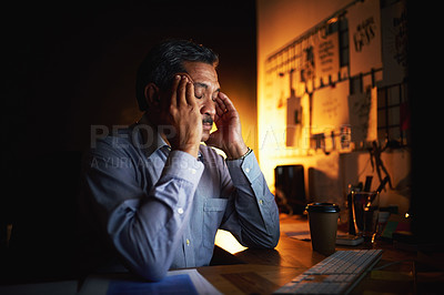 Buy stock photo Shot of a mature businessman looking stressed out while working late in an office