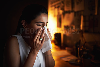 Buy stock photo Shot of a young businesswoman blowing her nose while working late in an office